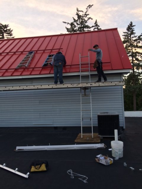Two men on a ladder working on a red metal roof