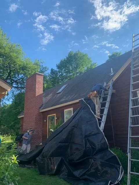 A man climbing up a ladder to the roof of a small brick house